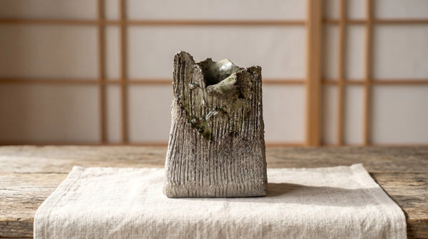 Textured ceramic surface with pale flecks and flowing green-amber glaze.