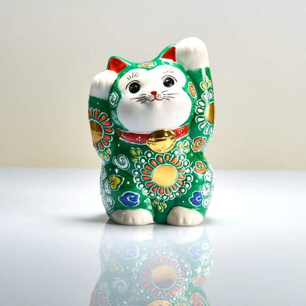 Front view of a deep green Kutani porcelain maneki neko with both paws raised, multicolored floral motifs, a red collar and a gold-tone bell-shaped ornament