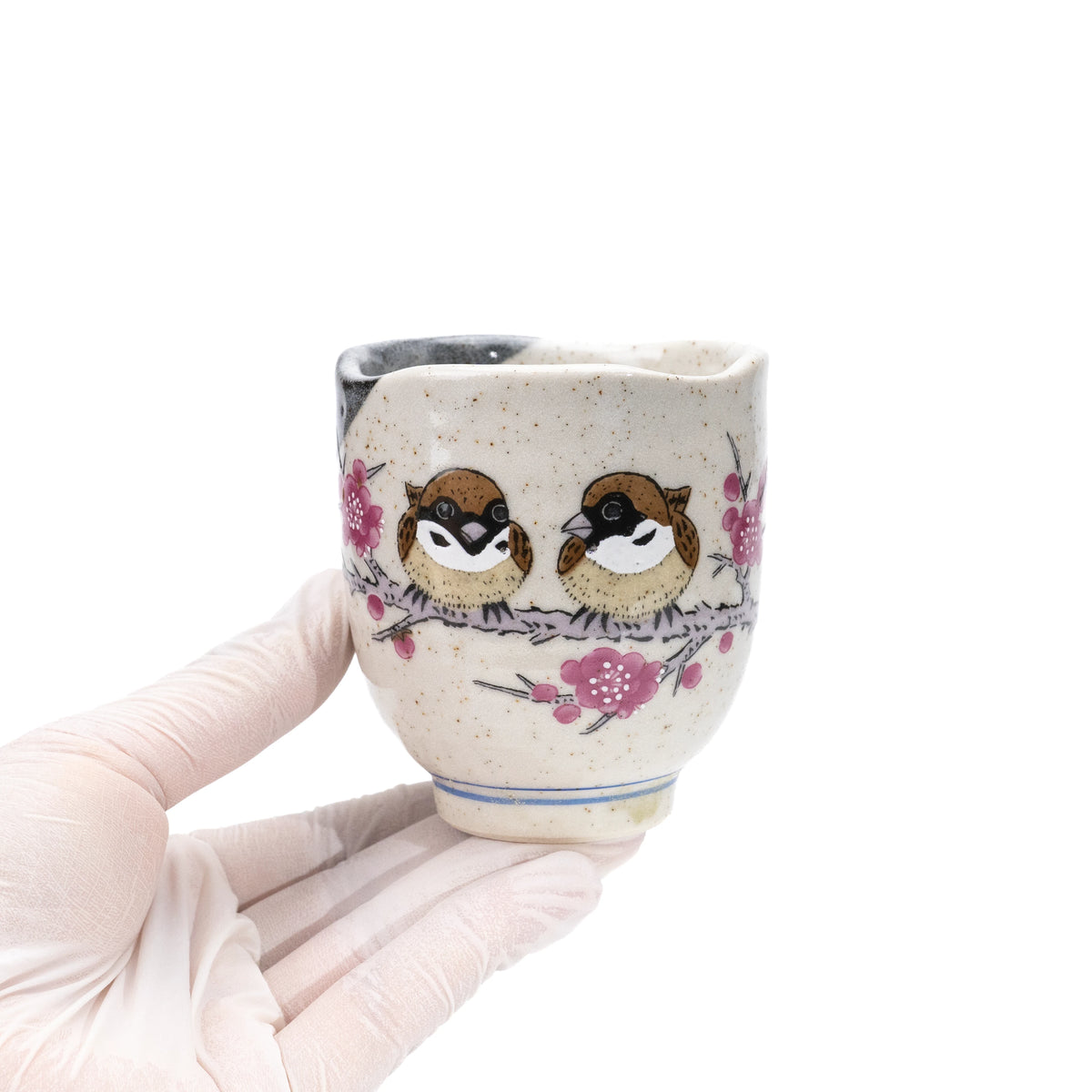Sparrow yunomi held in a gloved hand, showing its handleless shape and pink floral design.