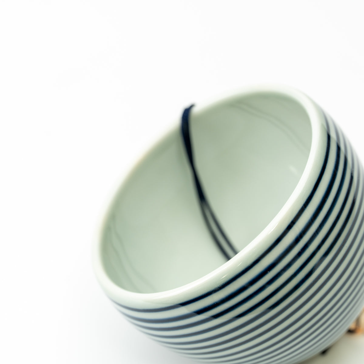Angled detail of the striped Arita wind-chime bell's smooth pale interior and rounded rim.