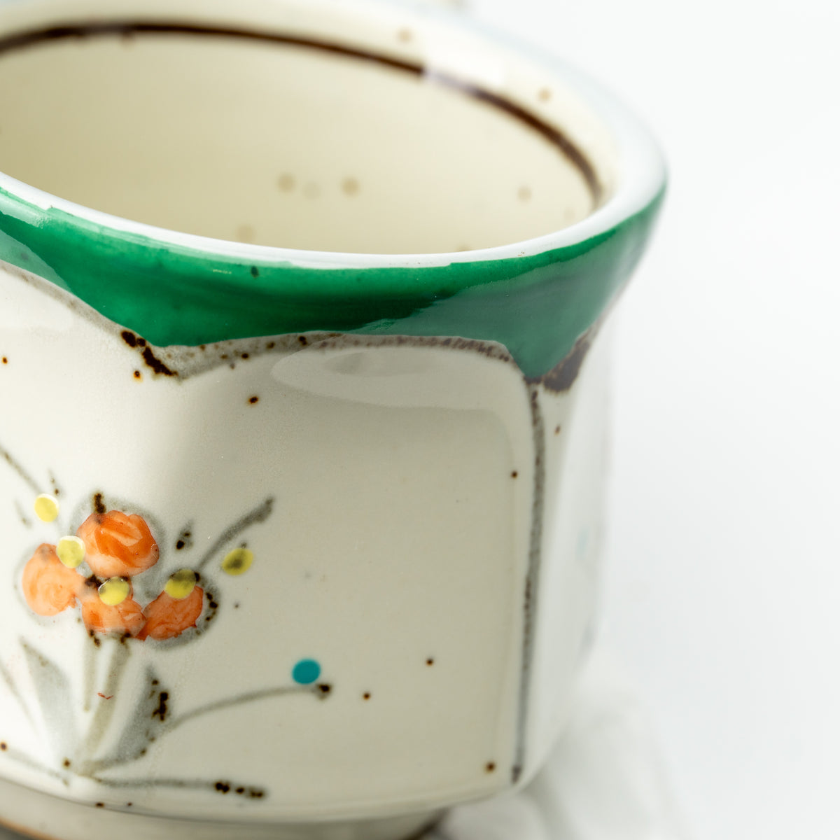Detail of the green-rimmed demitasse cup with an orange flower and fine dark outlines.