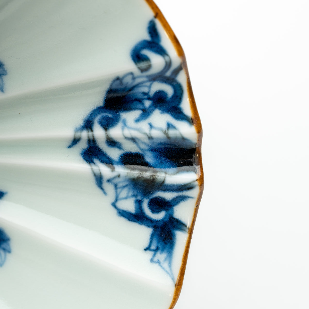 Close-up of blue scrolling foliage and the brown-edged fluted rim of the white karakusa bowl.