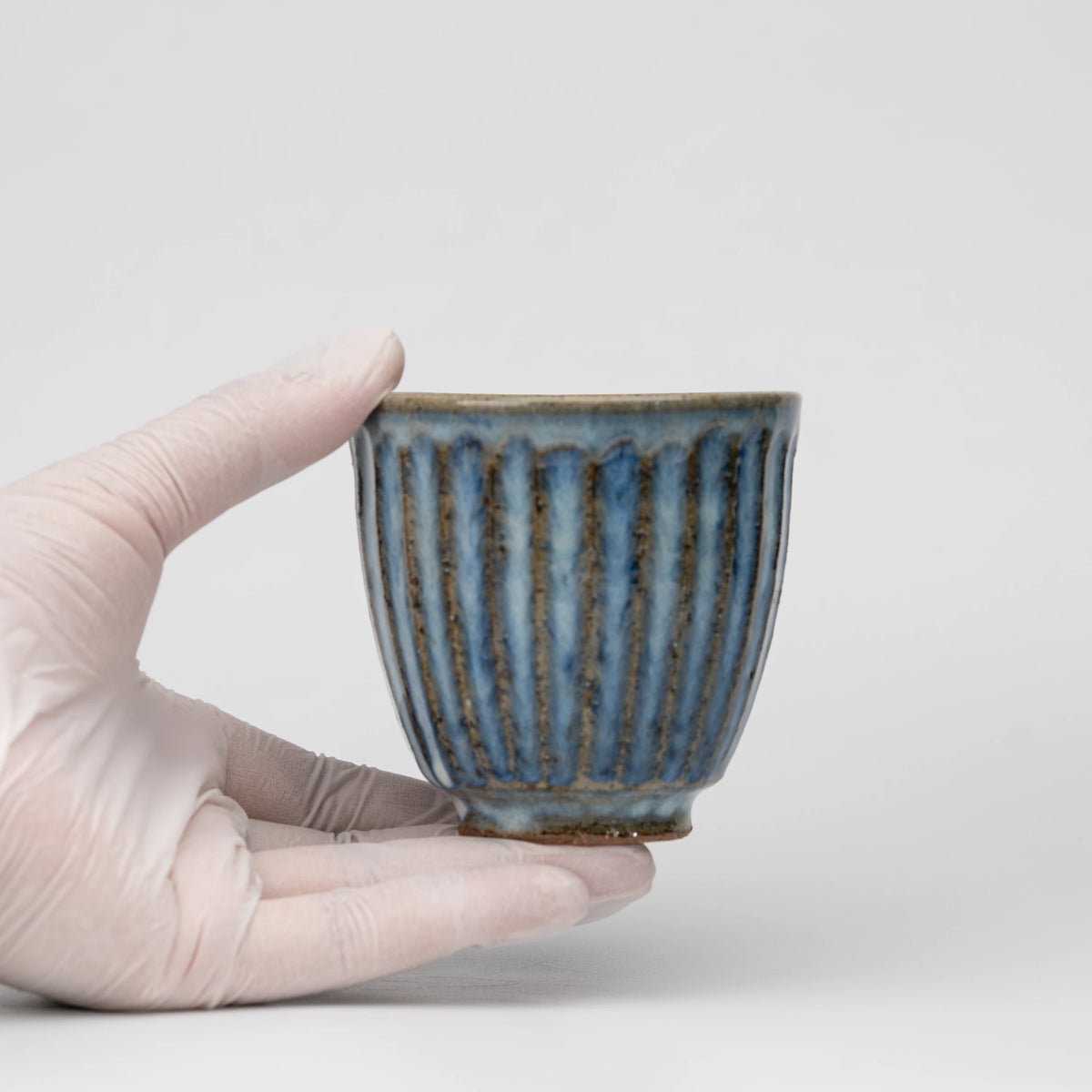 Ribbed blue-grey tea cup, held in a hand to show scale.