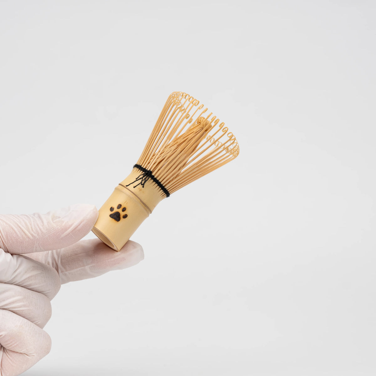 Paw-print bamboo mini whisk, held in a hand to show scale.