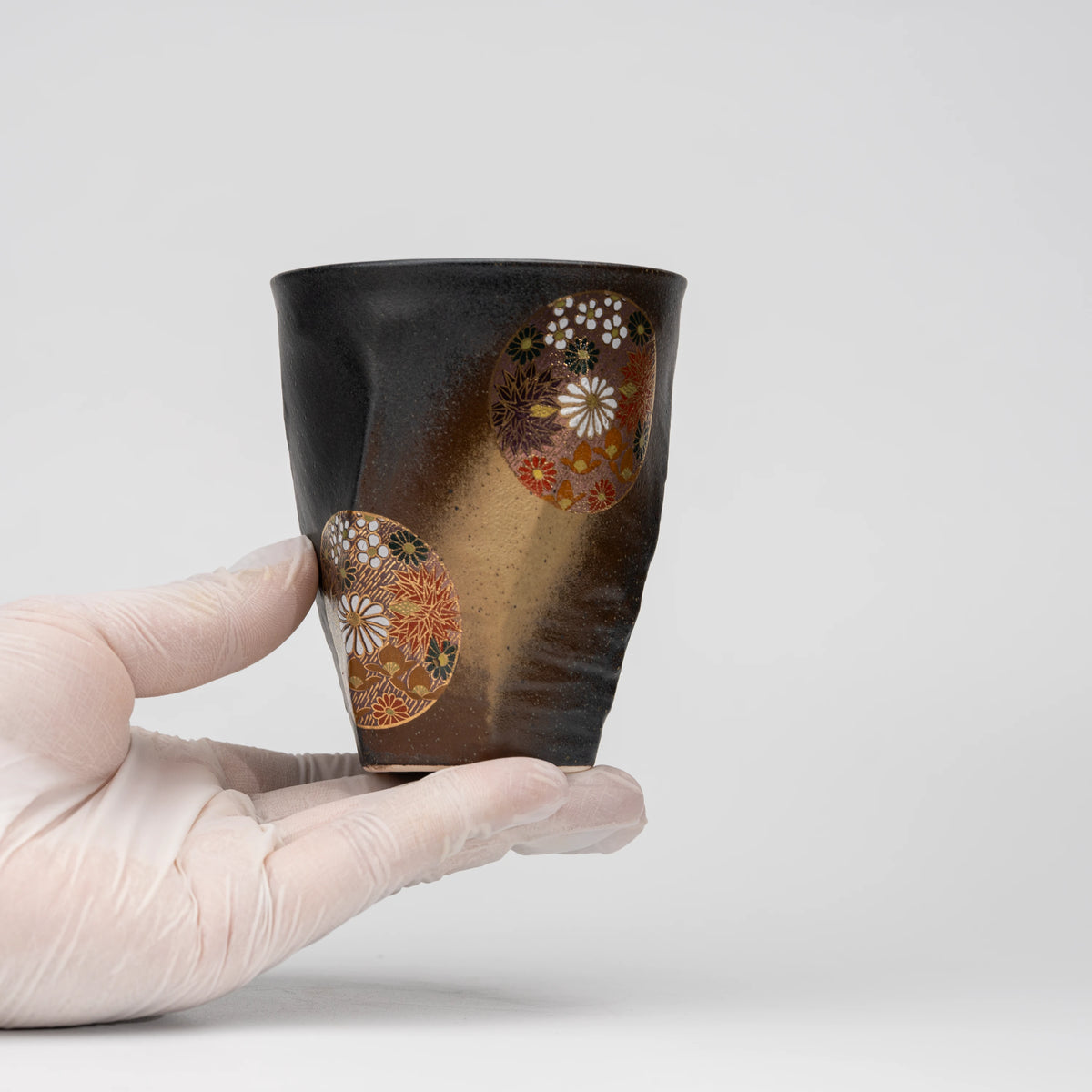 Dark floral medallion cup, held in a hand to show scale.