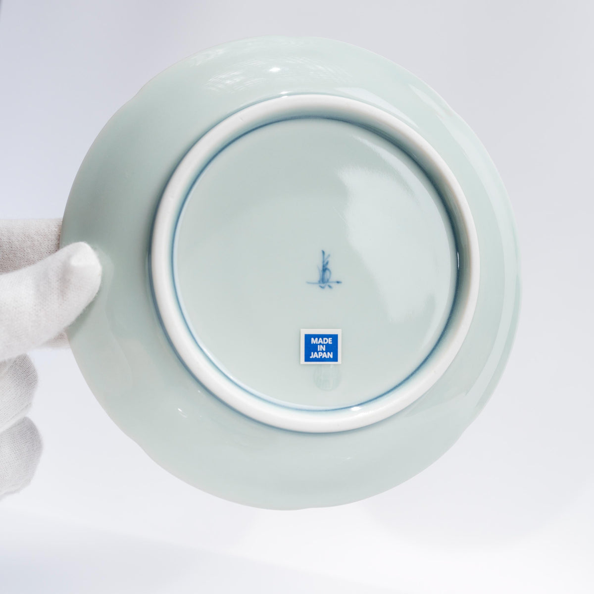 Underside of the matching saucer held in a gloved hand, showing its blue mark