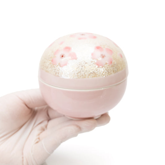 Round pink cherry blossom lidded bowl held in a gloved hand.