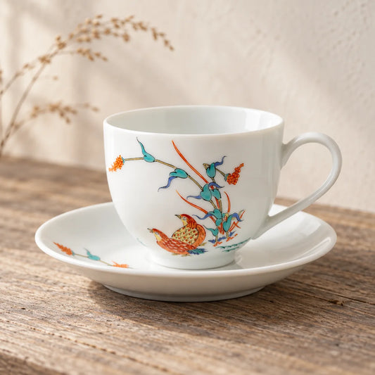 Hand-painted Arita quail cup resting empty on its matching saucer on a quiet wood table.