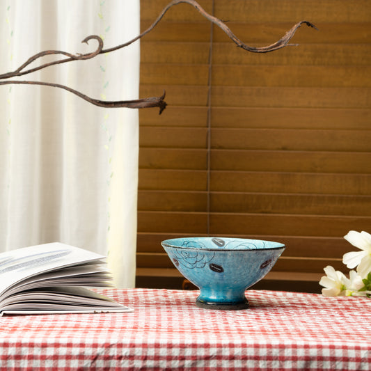 Turquoise rose dessert bowl on a red checked tablecloth beside a book.