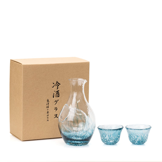 Blue glass sake carafe and two cups beside a brown presentation box.