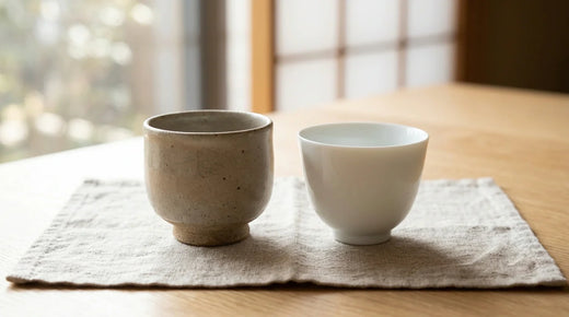 A matte stoneware cup beside a glossy white porcelain cup on linen, showing the two materials side by side.