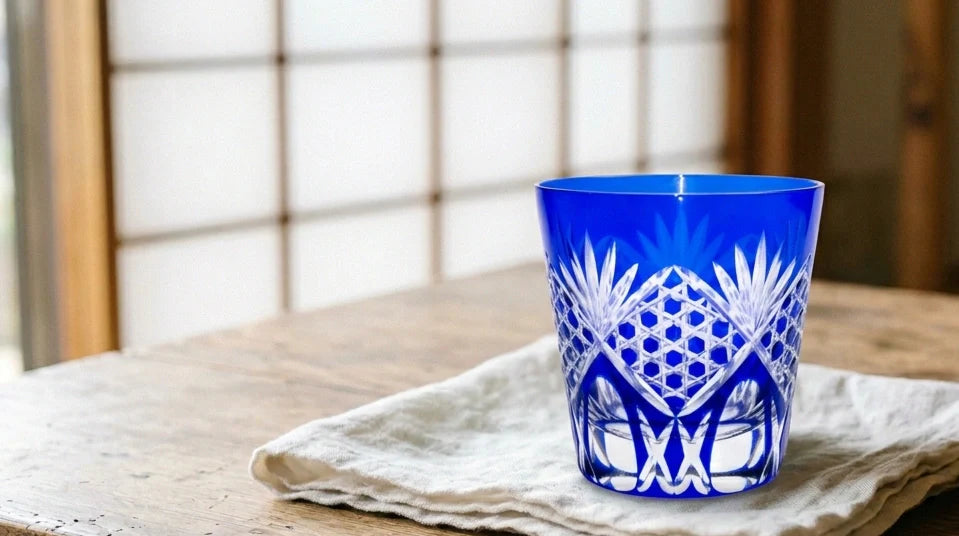 Ein Edo-Kiriko-Schliffglas mit facettiertem Muster, das das Licht einfängt, auf einer dunklen Holzfläche.
