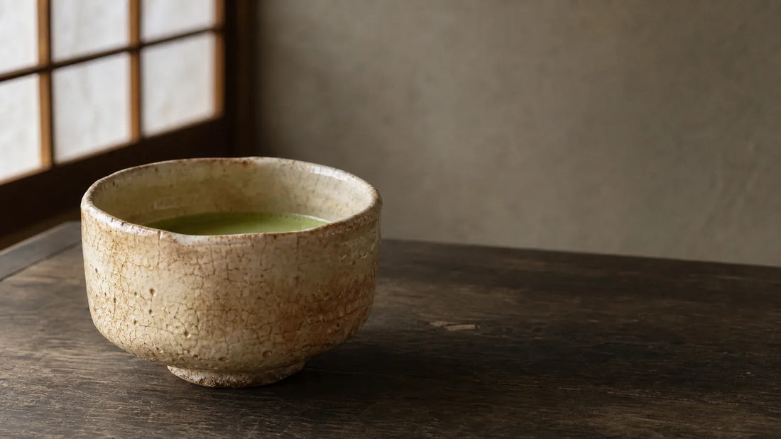 A well-used Hagi ware matcha bowl with amber patina and darkened glaze crazing on a wooden tea table.