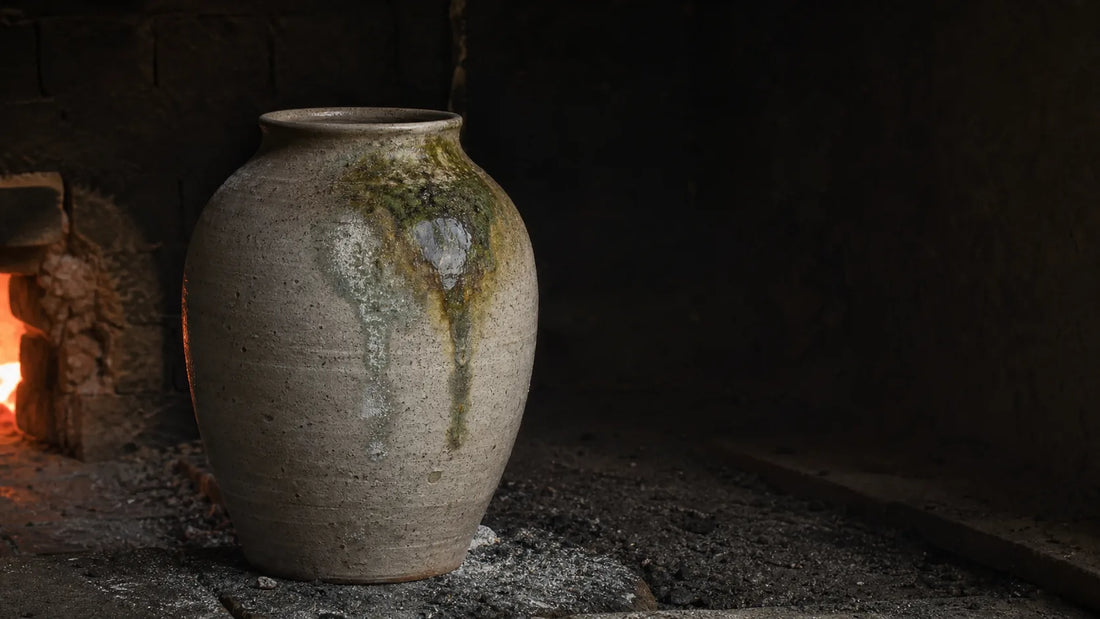 Ancient-style grey Sue ware jar with moss-green natural ash glaze inside a dark wood-fired kiln.