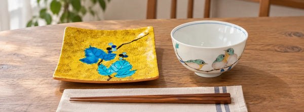Yellow wild-grape Kutani plate and white mejiro rice bowl on a sunlit wooden dining table.