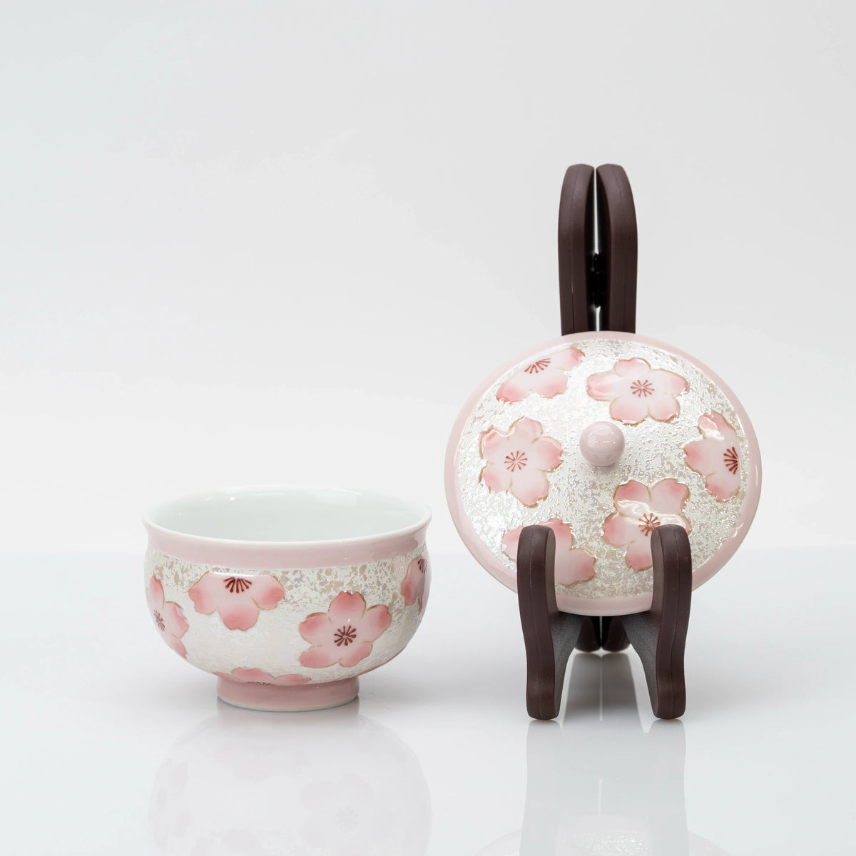 Open pink cherry blossom teacup beside its matching lid on a dark display stand, showing the floral decoration on both pieces.