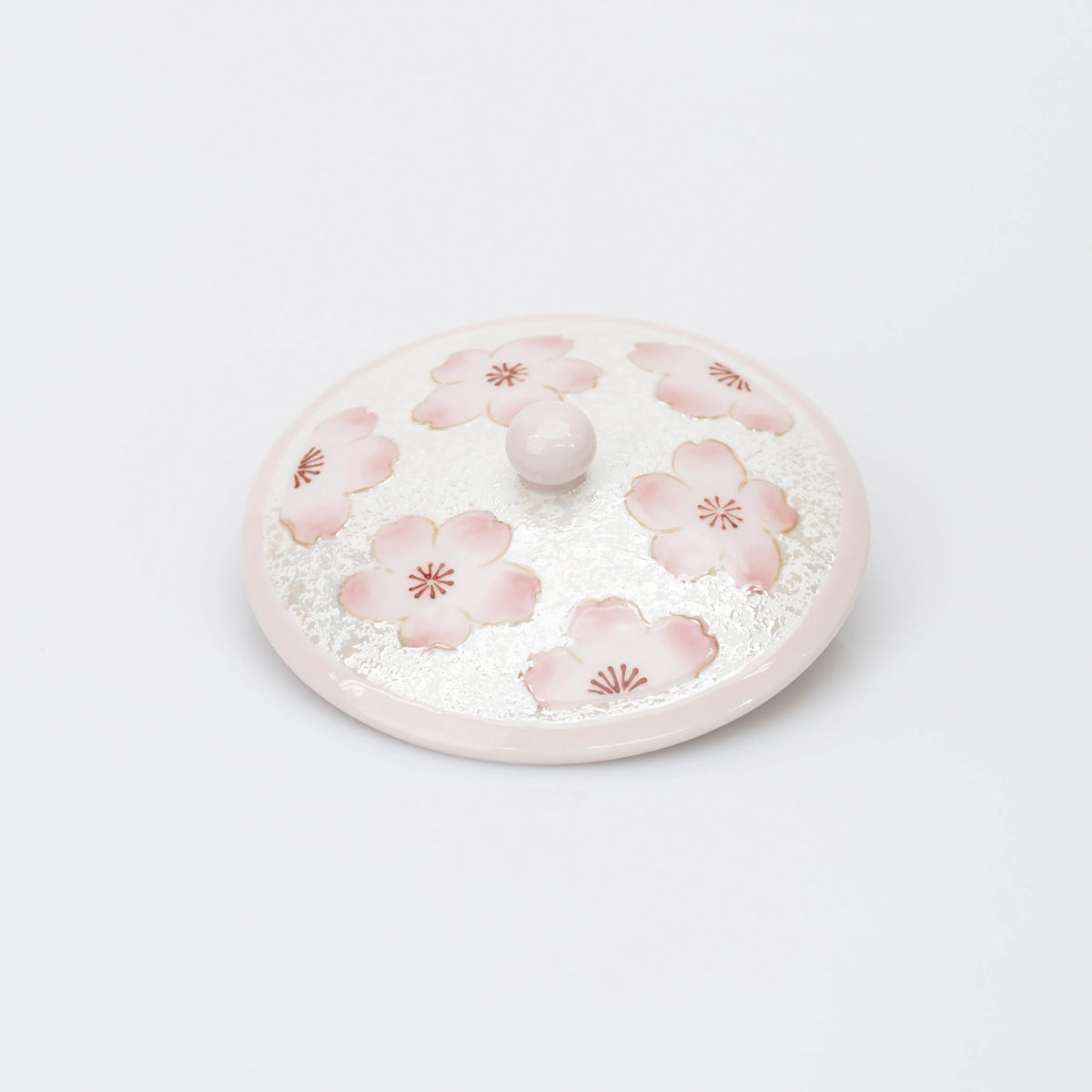 Top view of the teacup lid, decorated with pink cherry blossoms on a pearly white ground, with a rounded pink knob.