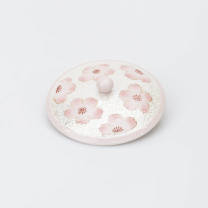 Top view of the teacup lid, decorated with pink cherry blossoms on a pearly white ground, with a rounded pink knob.