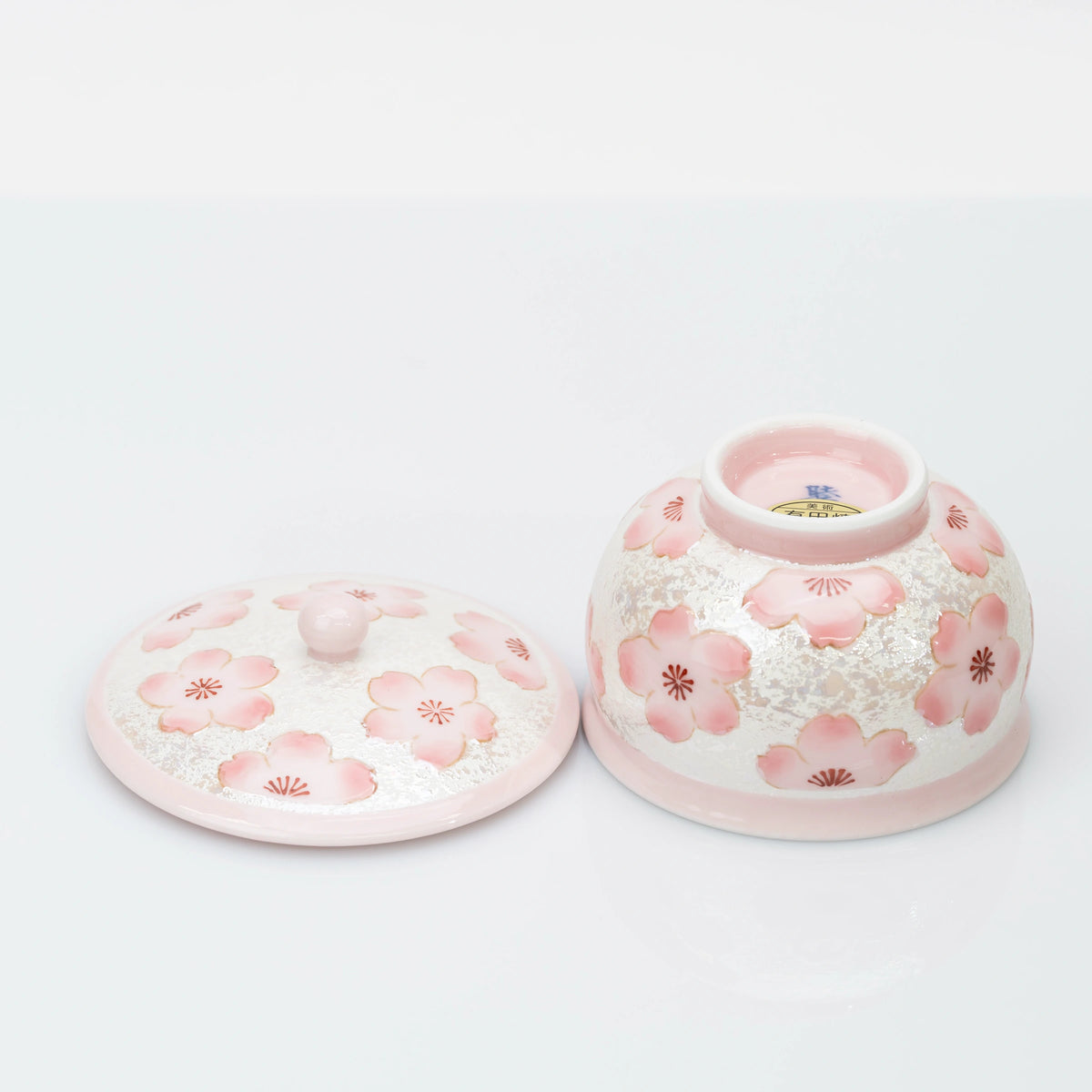 Upside-down cherry blossom teacup beside its lid, showing the foot ring, underside mark, and product label.