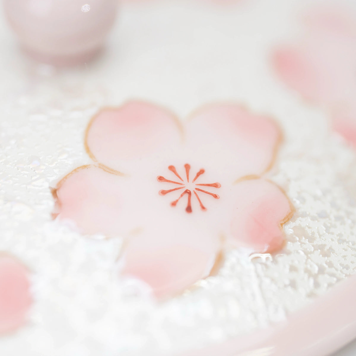 Close-up of a pink cherry blossom with fine petal outlines and a red center against the shimmering white finish.