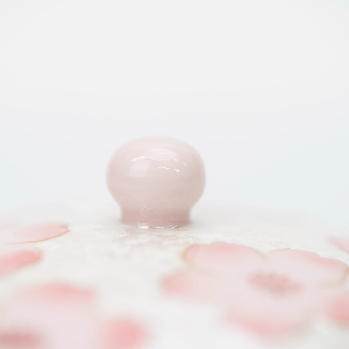 Close-up of the rounded pale pink lid knob, with pink cherry blossom petals and the pearly white finish below.