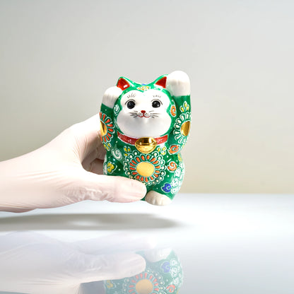 A gloved hand holding the 12 cm tall green Kutani beckoning cat to demonstrate its size and scale.