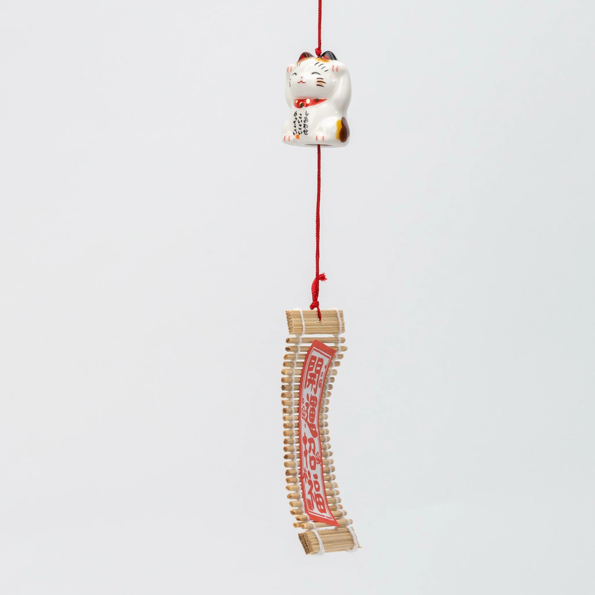 The chime hanging, red braided cord running from the parent bell through the kitten to the wind catcher