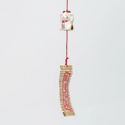The chime hanging, red braided cord running from the parent bell through the kitten to the wind catcher