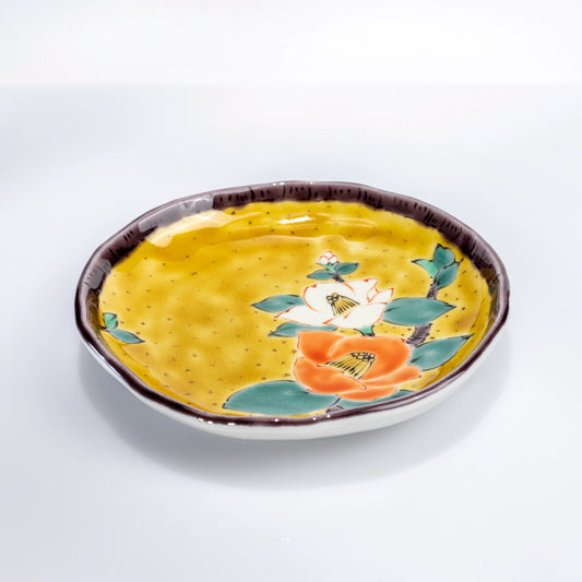 Angled view of a Kutani yellow dessert plate with hand-painted camellia motif
