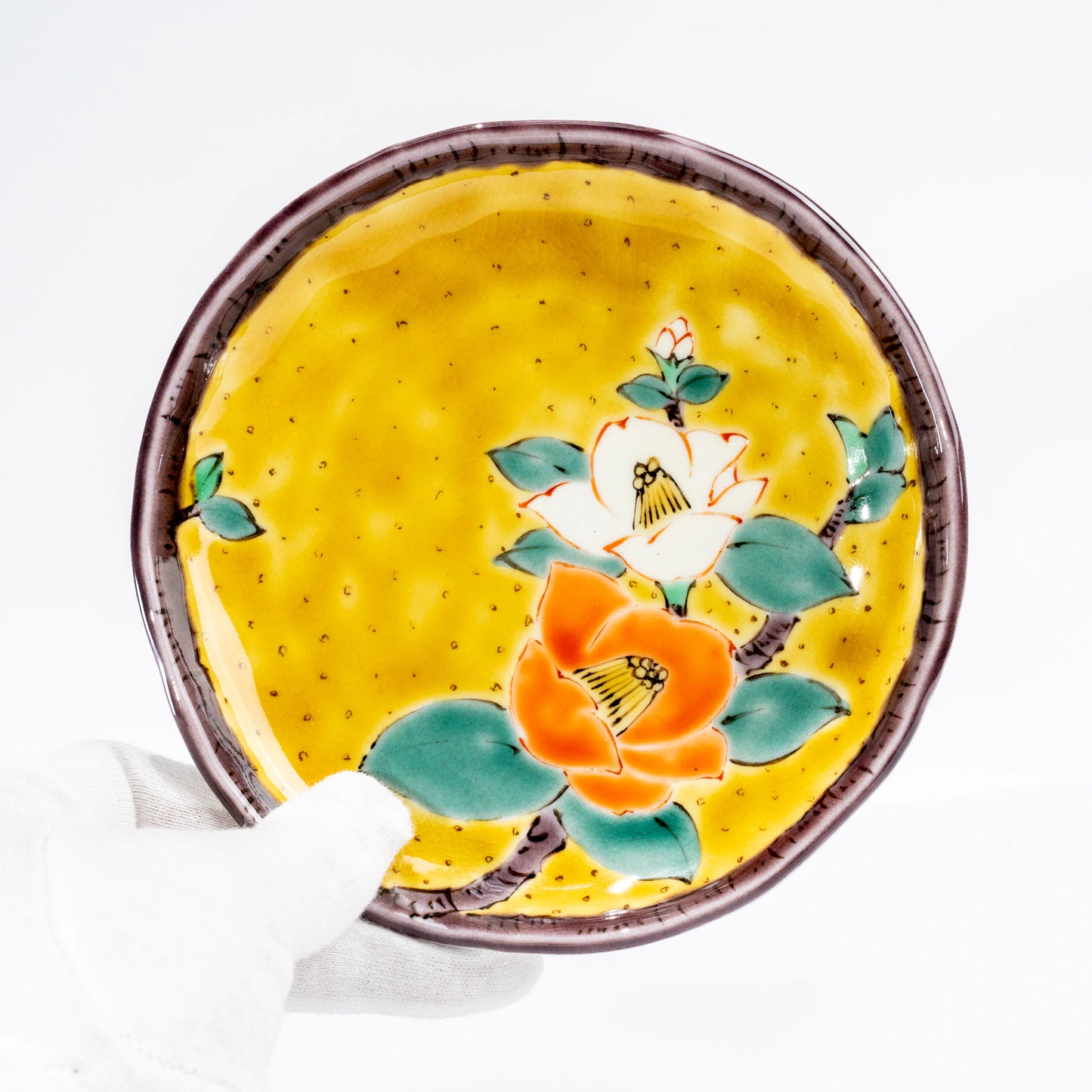 Close-up of a Kutani yellow dessert plate with hand-painted camellia design
