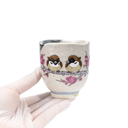 Sparrow yunomi held in a gloved hand, showing its handleless shape and pink floral design.