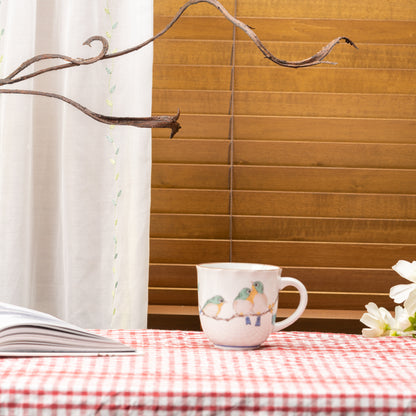 Mejiro bird mug on a red gingham tablecloth beside an open book and white flowers.