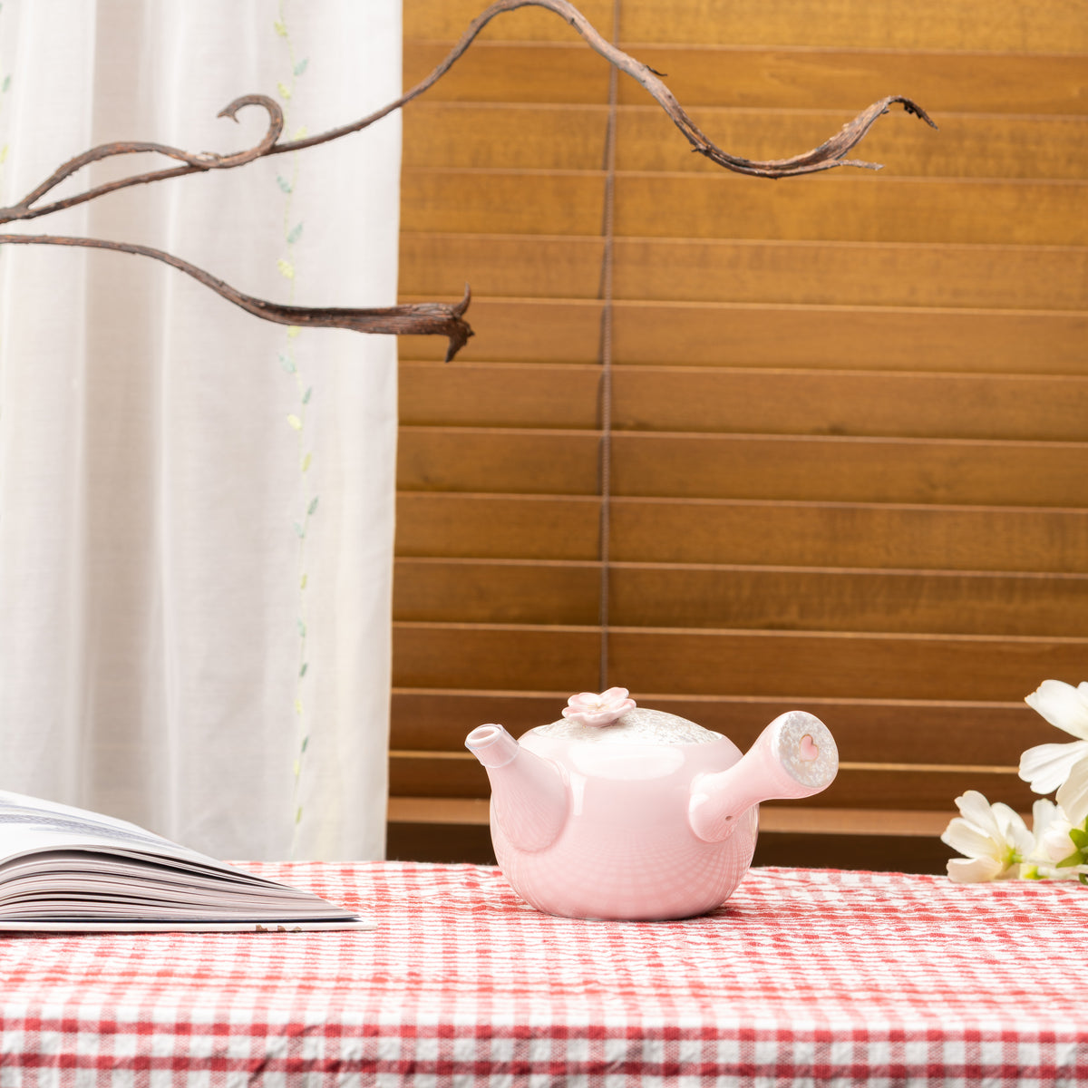 Pink Sakura kyusu teapot on a red gingham tablecloth beside an open book and flowers.