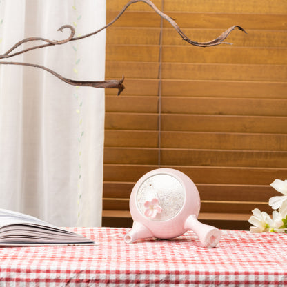 Pink Sakura kyusu teapot tilted on its side to show the floral lid on a red gingham tablecloth.