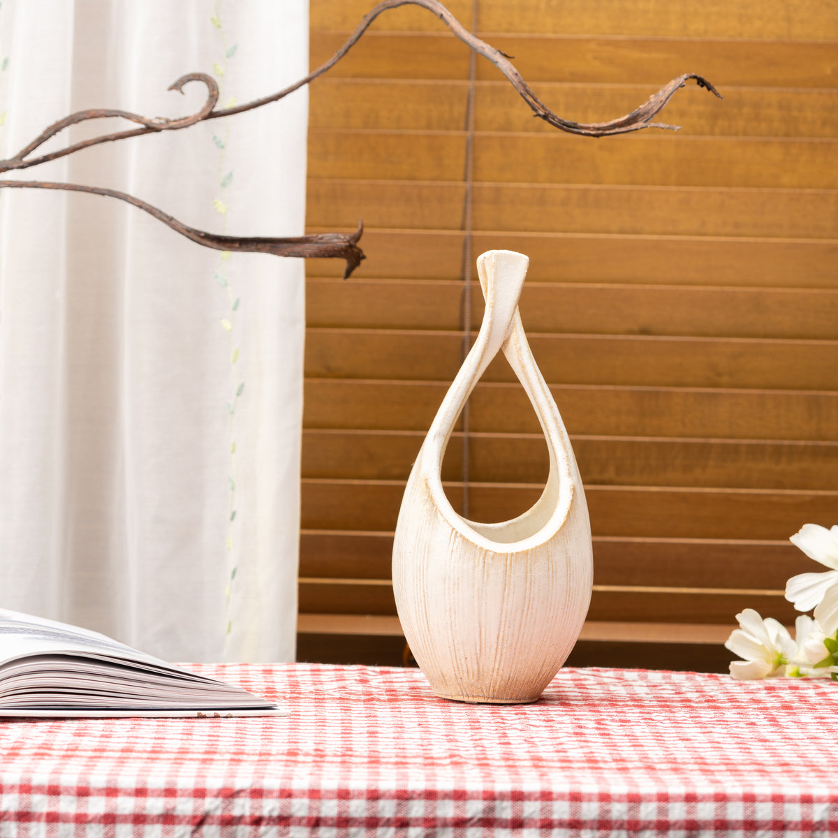 Tall cream-colored Kairo loop vase on a red gingham tablecloth beside a window.