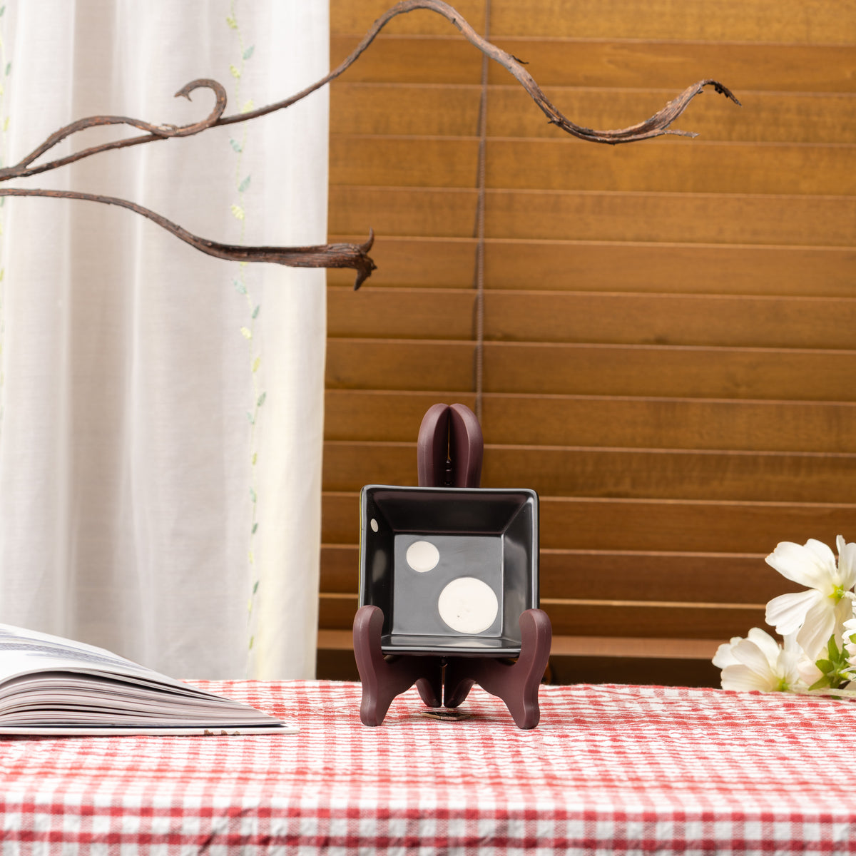 Black Mino bowl with two pale circles displayed upright on a stand on red gingham.