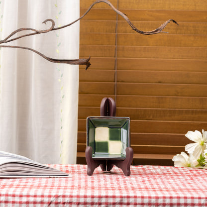 Green-and-cream checkerboard Mino bowl displayed upright on a stand on red gingham.