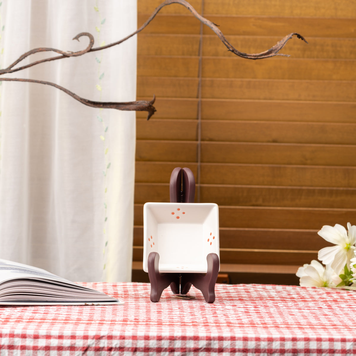 White Mino bowl with small orange dot clusters displayed upright on a stand on red gingham.