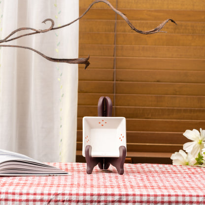 White Mino bowl with small orange dot clusters displayed upright on a stand on red gingham.