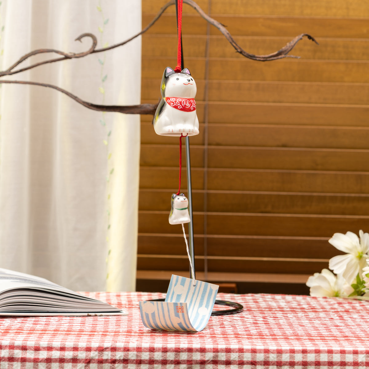 Black-and-white Shiba parent and puppy wind chime with a red bib, hanging beside a window.