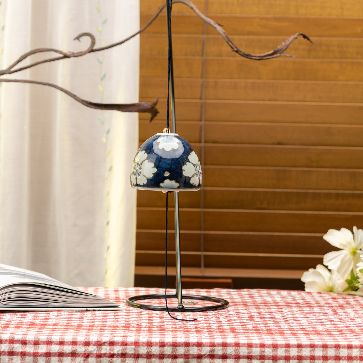 Blue-and-white floral wind chime hanging from a branch above a red gingham tablecloth.