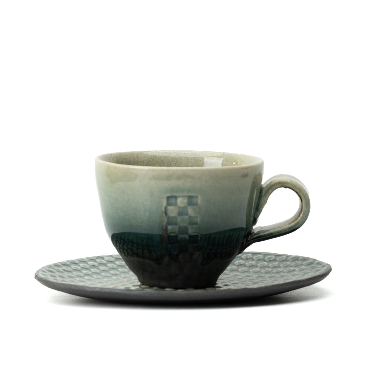 Green-to-dark Hechimon Mosaic cup on its checkered saucer with the handle to the right.