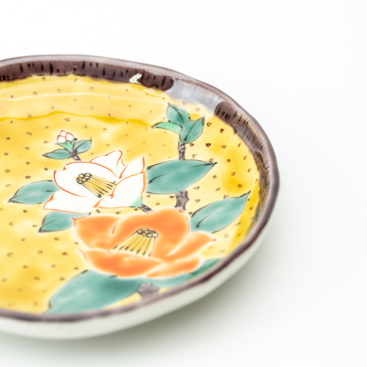 Close-up of orange and white camellias with green leaves on the yellow Kutani plate.
