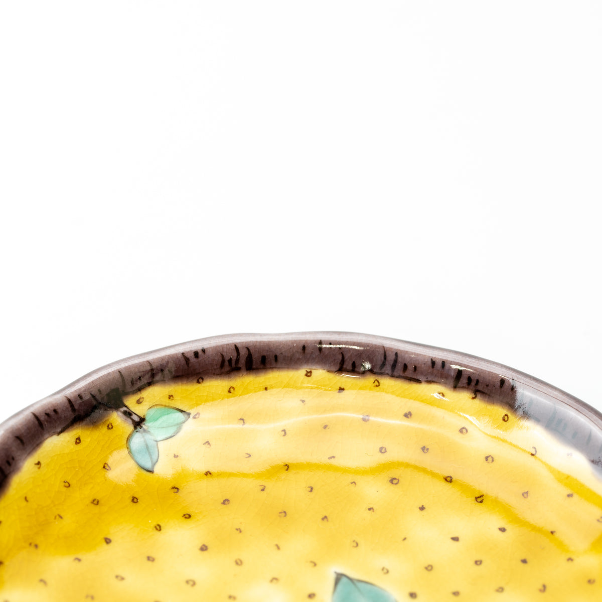 Close-up of the yellow camellia plate's dark rim and dotted yellow glaze.