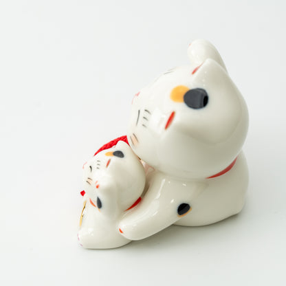 Side view of the calico parent lucky cat holding a kitten, showing the black and orange markings.
