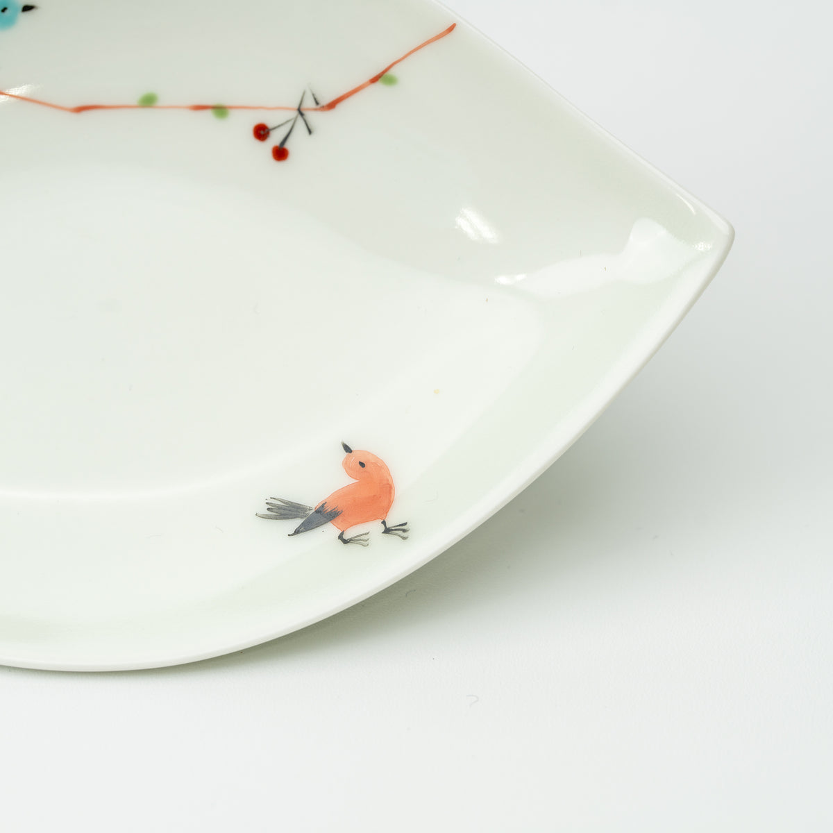 Detail of an orange bird and a branch with small red berries on the white leaf-shaped plate.
