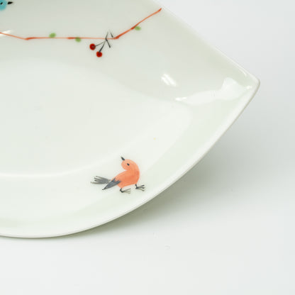 Detail of an orange bird and a branch with small red berries on the white leaf-shaped plate.