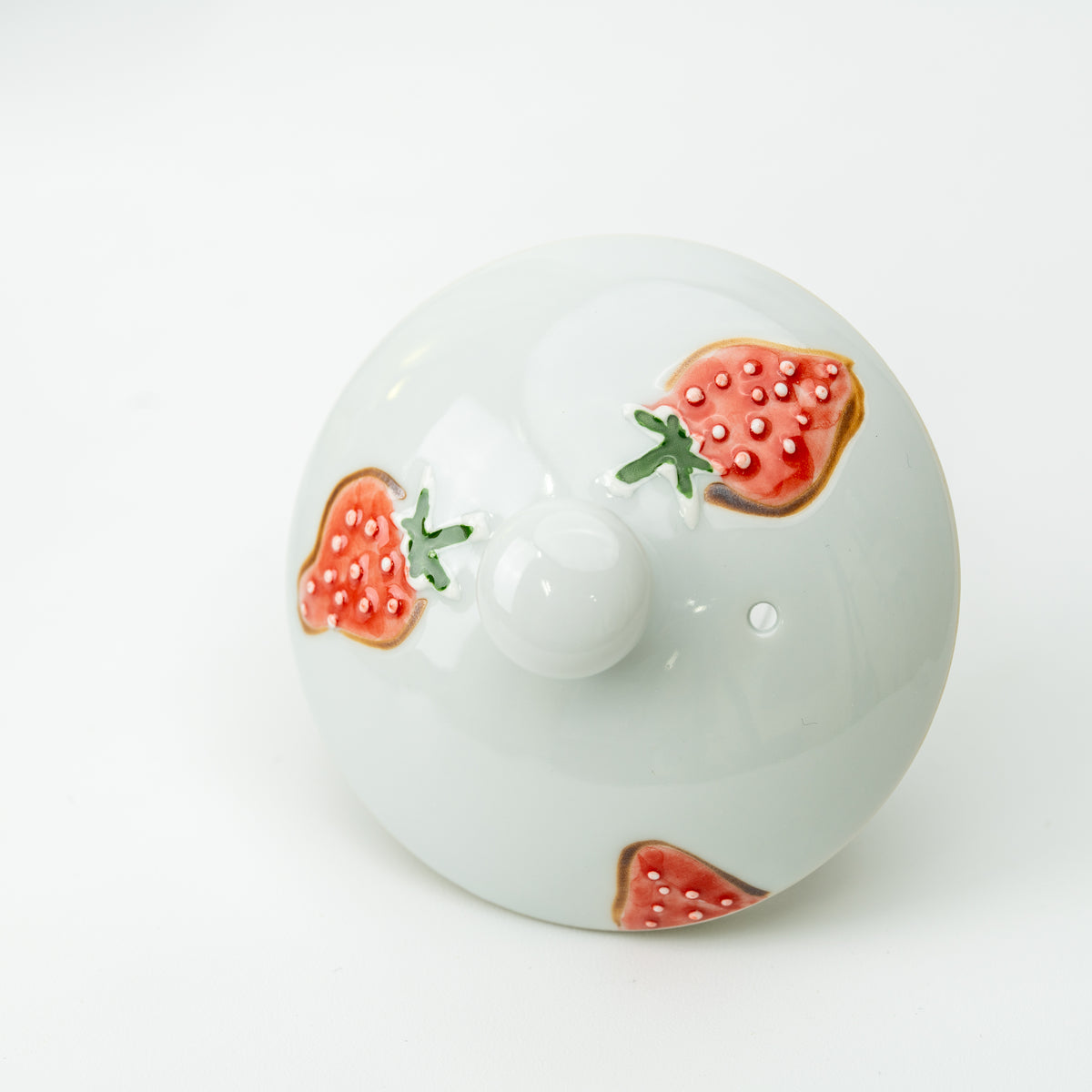 Top view of the strawberry teapot lid showing red strawberries, a round knob and steam hole.