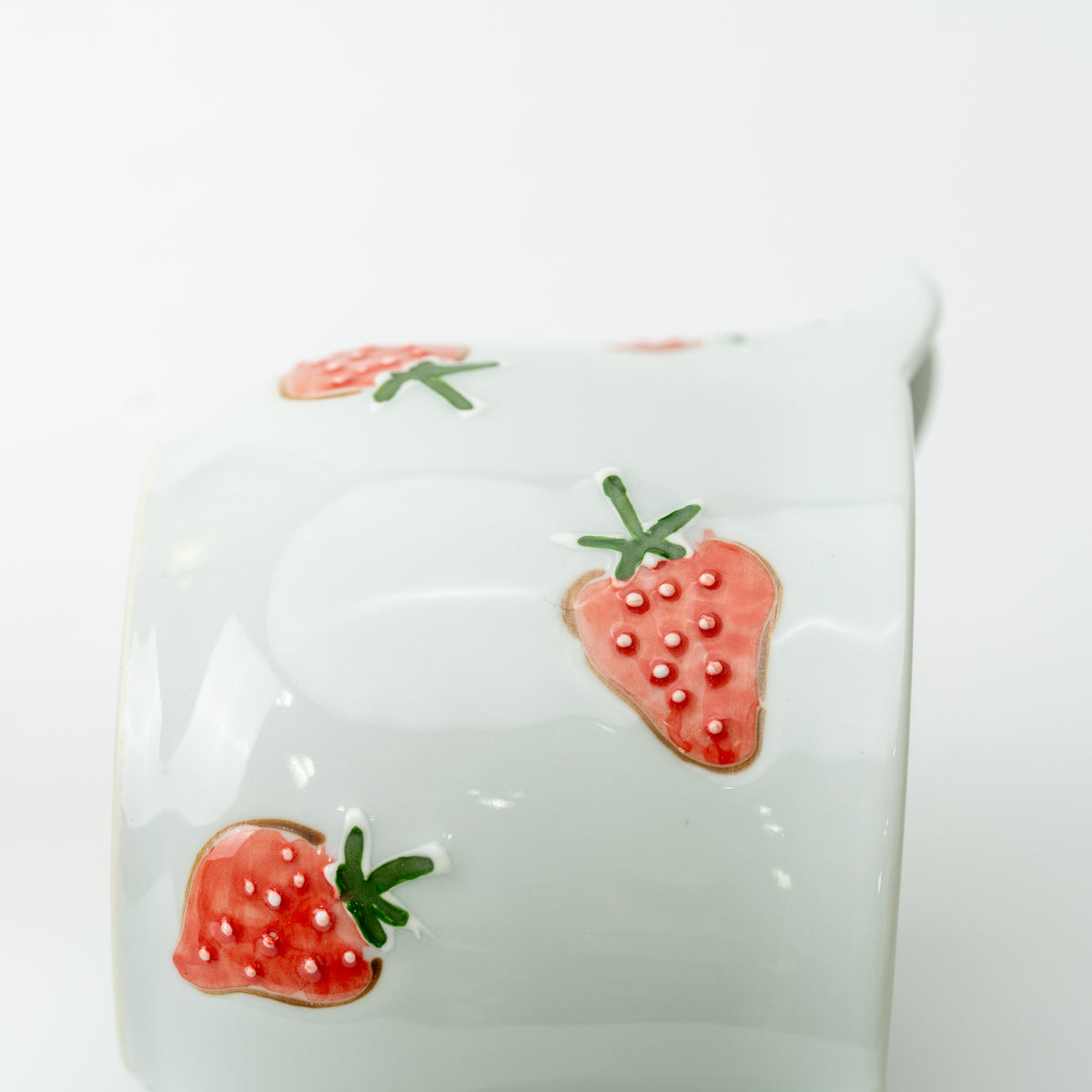 Detail of two raised red strawberries beneath the spout of the white Tokushichi teapot.