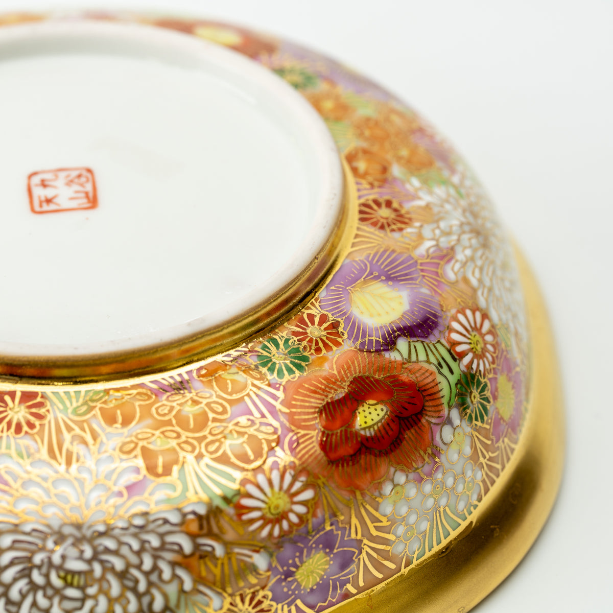 Underside detail of the Kinhanazume serving bowl, showing a red maker's mark surrounded by floral decoration.